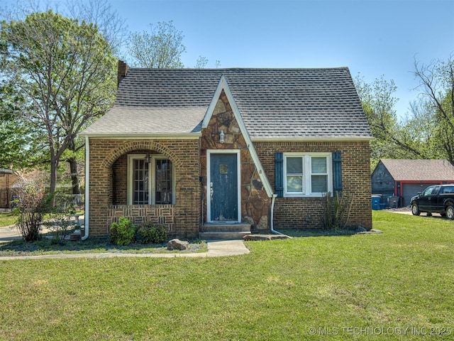 tudor home with brick siding, roof with shingles, a front yard, and covered porch
