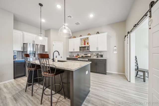 13010 E 125th Pl N, Collinsville, OK 74021 - kitchen featuring a barn door, appliances with stainless steel finishes, a kitchen bar, light wood-style flooring, and white cabinetry