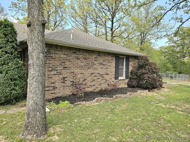 view of home's exterior with a yard, brick siding, fence, and roof with shingles