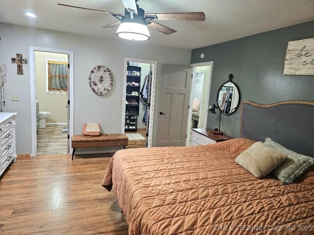 bedroom with light wood finished floors, ensuite bathroom, a spacious closet, a closet, and ceiling fan