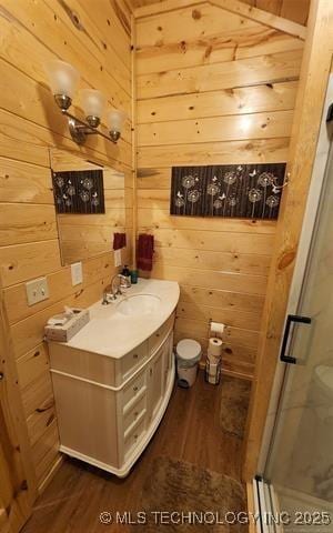 full bath with a shower stall, wooden walls, toilet, wood finished floors, and vanity