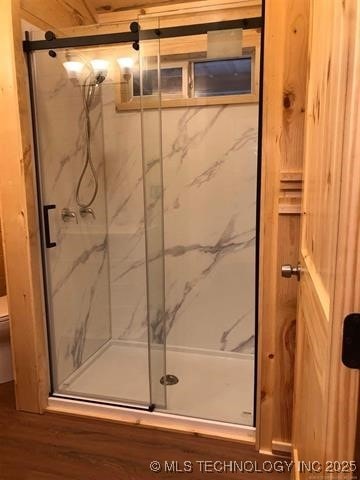 full bath featuring wood finished floors, toilet, and a marble finish shower