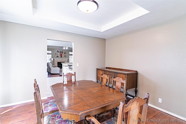 dining area with hardwood / wood-style flooring, baseboards, a tray ceiling, and a fireplace