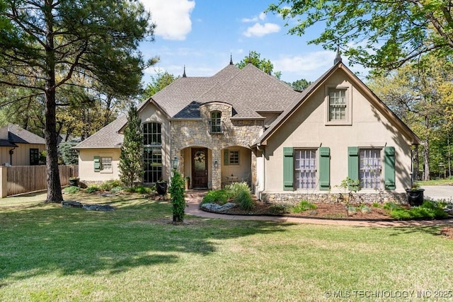 french country style house with stucco siding, fence, a front yard, and stone siding