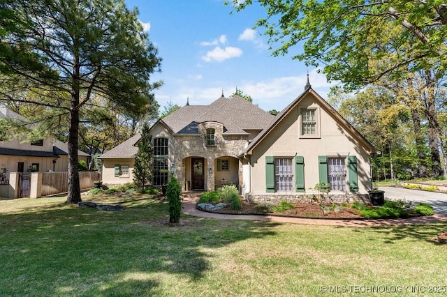 french provincial home with fence, stucco siding, a front yard, and stone siding