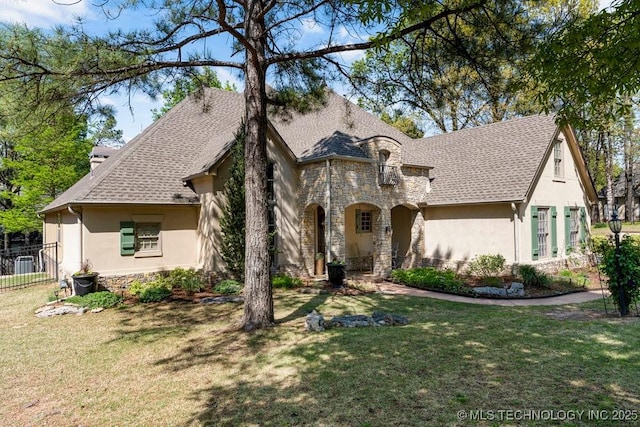 french country home featuring a front lawn, stone siding, stucco siding, and fence