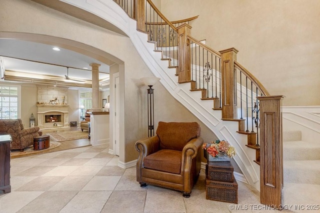 stairway featuring tile patterned floors, ornate columns, arched walkways, and a warm lit fireplace