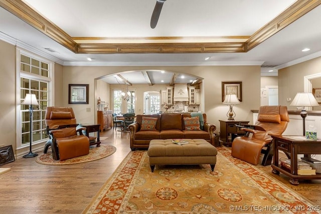 living room with a raised ceiling, arched walkways, wood finished floors, and crown molding