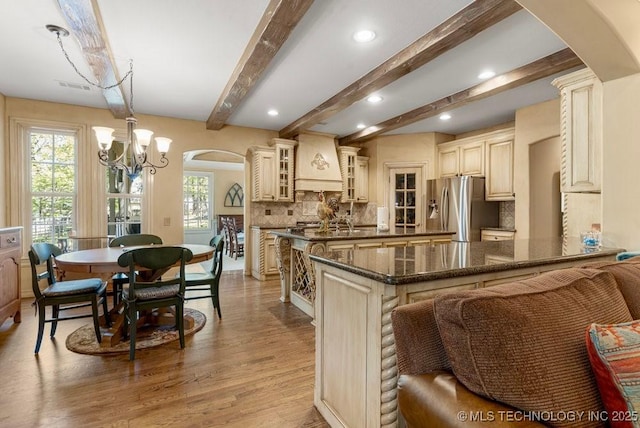kitchen featuring custom range hood, cream cabinets, stainless steel fridge, and arched walkways