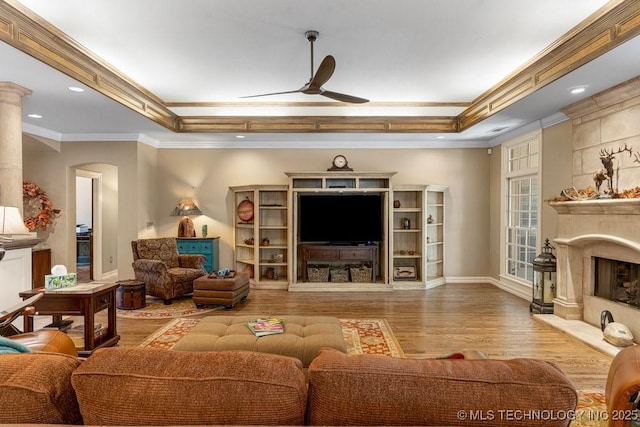 living room featuring ceiling fan, wood finished floors, ornamental molding, arched walkways, and a high end fireplace