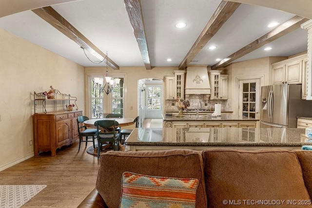 kitchen with baseboards, premium range hood, arched walkways, wood finished floors, and stainless steel fridge with ice dispenser