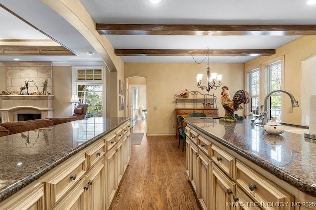 kitchen with arched walkways, beam ceiling, wood finished floors, and a fireplace