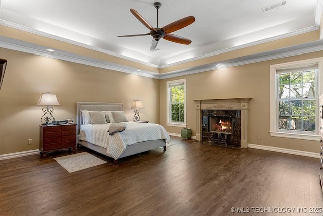 bedroom with wood finished floors, visible vents, a tray ceiling, and multiple windows