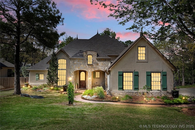 french country style house with fence, stucco siding, a front yard, and stone siding