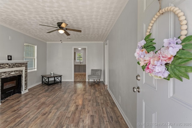 interior space featuring wood finished floors, ceiling fan, a fireplace, baseboards, and ornamental molding