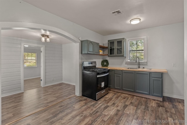 kitchen with arched walkways, a sink, dark wood-style flooring, visible vents, and gas range oven
