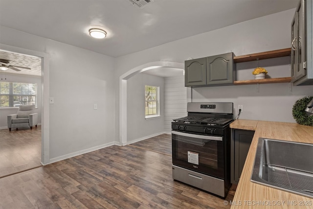 kitchen featuring arched walkways, dark wood-type flooring, baseboards, gas range, and ceiling fan
