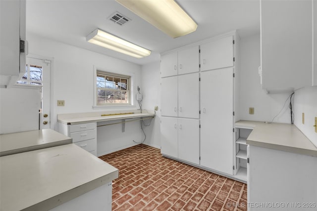 kitchen with brick floor, light countertops, visible vents, and a healthy amount of sunlight