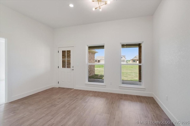 spare room with light wood-style flooring, baseboards, and a chandelier