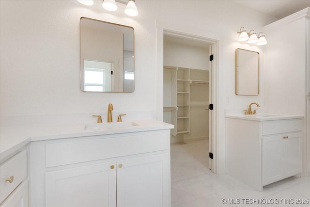 bathroom with two vanities, a spacious closet, and a sink