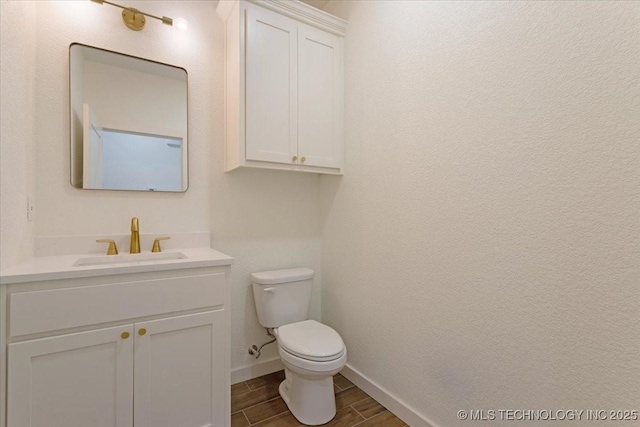 half bathroom with baseboards, wood finish floors, toilet, and vanity