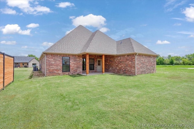 rear view of property with brick siding, a lawn, a shingled roof, and a patio