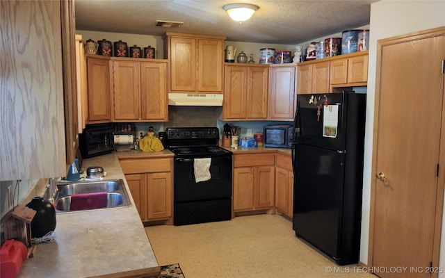 kitchen with a sink, visible vents, light countertops, under cabinet range hood, and black appliances