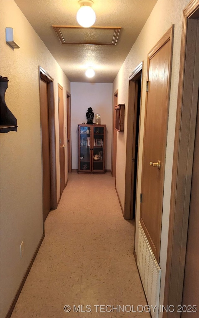 hallway with attic access, light floors, a textured ceiling, and visible vents