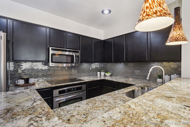 kitchen with a sink, decorative backsplash, dark cabinets, light stone countertops, and appliances with stainless steel finishes