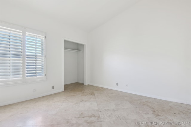 unfurnished bedroom with lofted ceiling, a closet, and baseboards