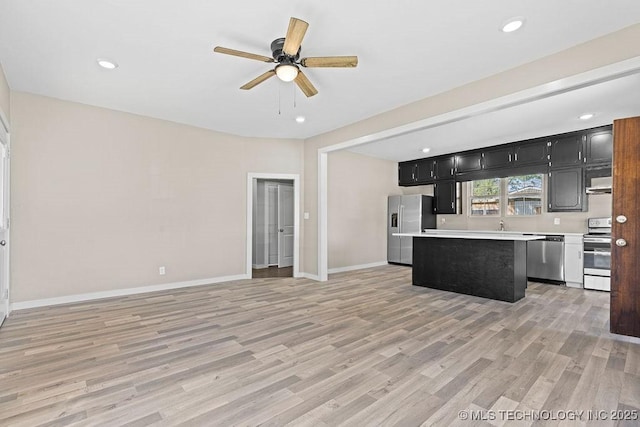 401 S Brewer St, Vinita, OK 74301 - kitchen featuring light countertops, dark cabinetry, light wood-type flooring, a center island, and appliances with stainless steel finishes