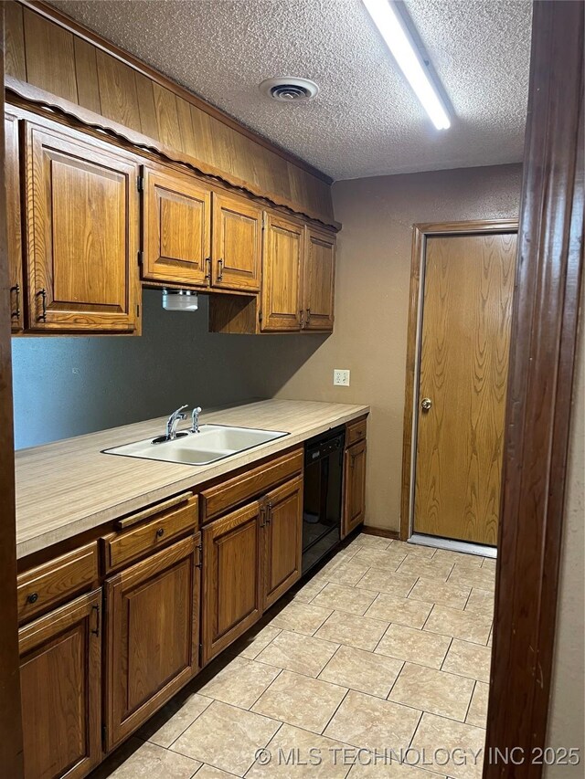 kitchen with a sink, light countertops, a textured ceiling, black dishwasher, and visible vents