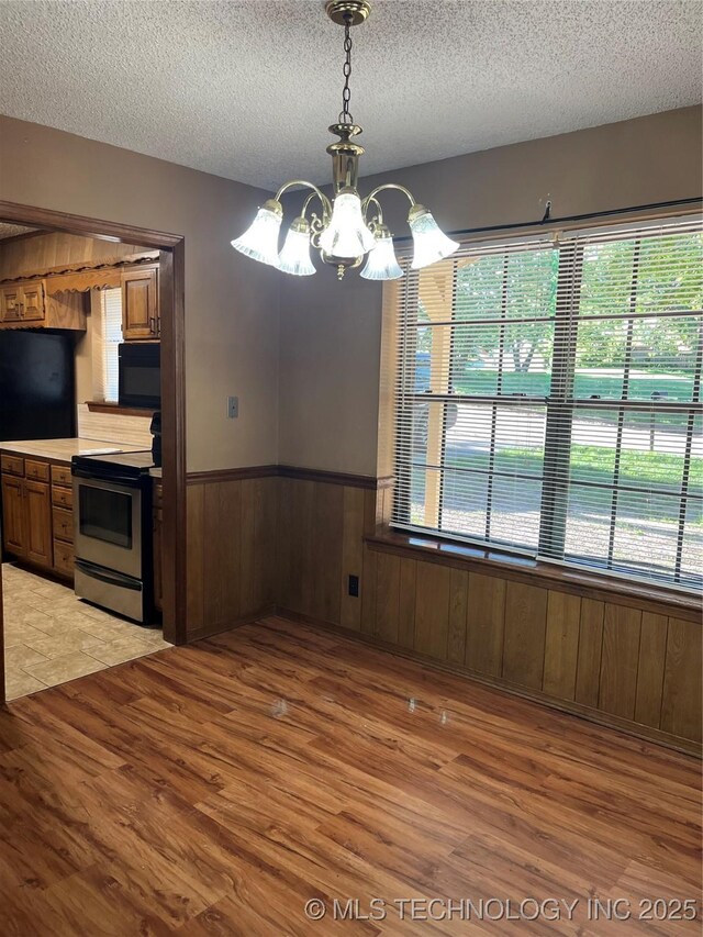 unfurnished dining area with a textured ceiling, light wood-style flooring, wainscoting, and a chandelier
