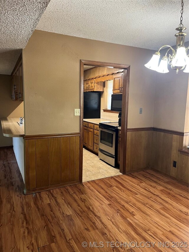 kitchen with electric range, a textured ceiling, black microwave, wainscoting, and an inviting chandelier