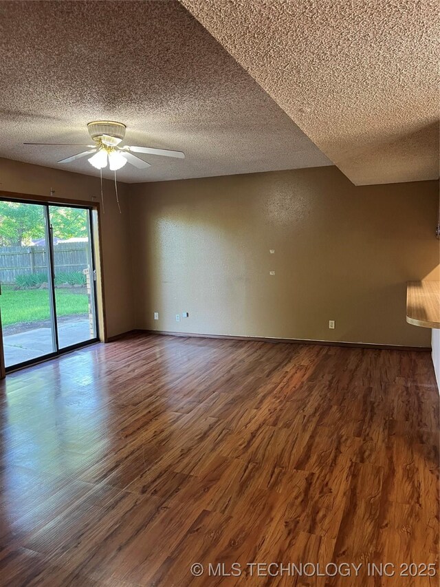 empty room featuring a ceiling fan, a textured ceiling, baseboards, and dark wood-type flooring