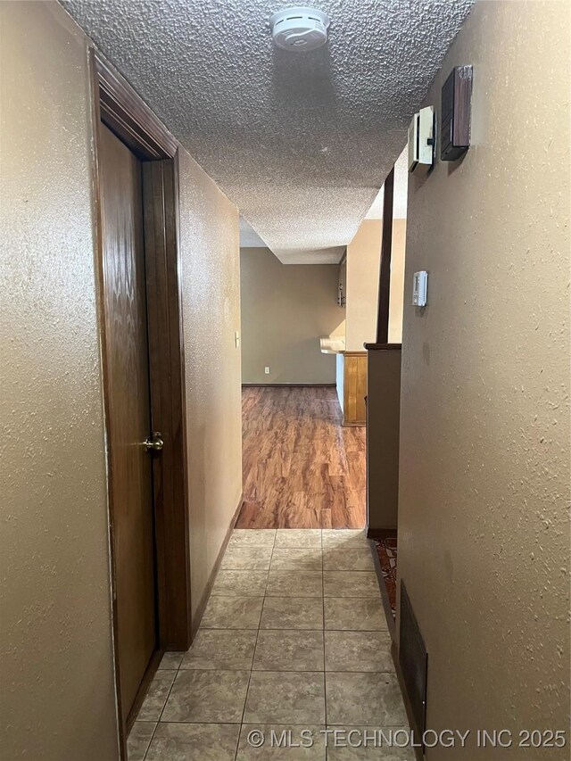 hall with a textured wall, a textured ceiling, and visible vents