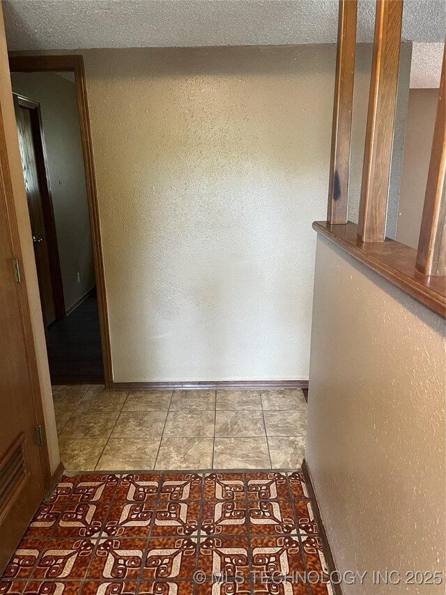 corridor with baseboards, a textured wall, tile patterned floors, and a textured ceiling