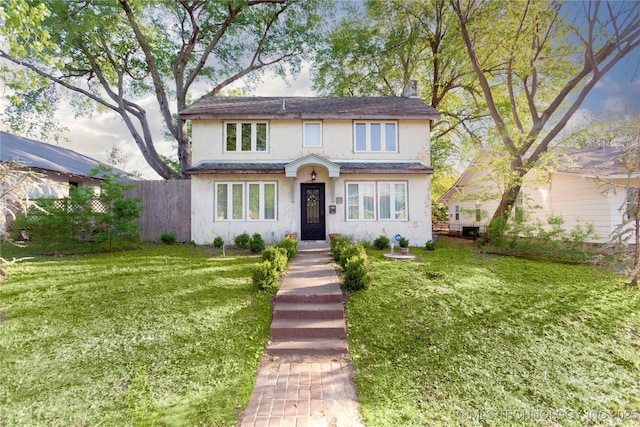 traditional-style house with fence, a front lawn, and stucco siding