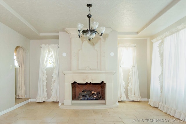 unfurnished living room featuring a wealth of natural light, a notable chandelier, a tray ceiling, and a textured ceiling