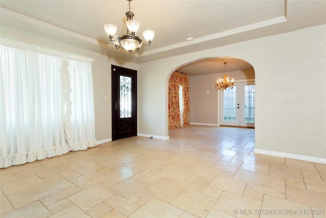 entrance foyer with stone tile flooring, a tray ceiling, arched walkways, baseboards, and a notable chandelier