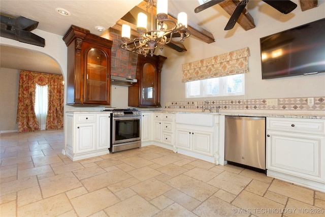 kitchen featuring stainless steel appliances, stone tile flooring, a sink, ceiling fan with notable chandelier, and under cabinet range hood