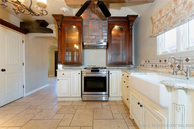 kitchen featuring stone tile flooring, arched walkways, a sink, gas stove, and under cabinet range hood