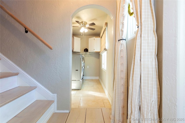 hall with arched walkways, baseboards, a textured wall, and stairs