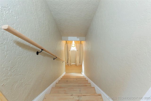 stairway featuring a textured wall, baseboards, wood finished floors, and a textured ceiling