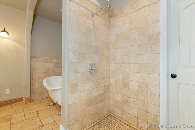 full bathroom featuring a stall shower, wainscoting, stone tile floors, tile walls, and a soaking tub