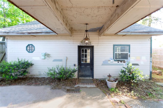 doorway to property featuring fence and a shingled roof