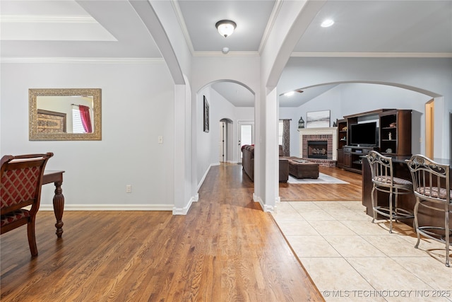 3235 Boardwalk Ct, Bartlesville, OK 74006 - entrance foyer with light wood-style flooring, arched walkways, baseboards, crown molding, and a fireplace