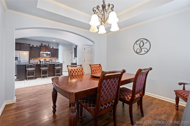 3235 Boardwalk Ct, Bartlesville, OK 74006 - dining area featuring light wood-style flooring, arched walkways, a chandelier, crown molding, and a raised ceiling