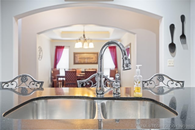 3235 Boardwalk Ct, Bartlesville, OK 74006 - kitchen with a tray ceiling, arched walkways, a sink, dark stone counters, and an inviting chandelier