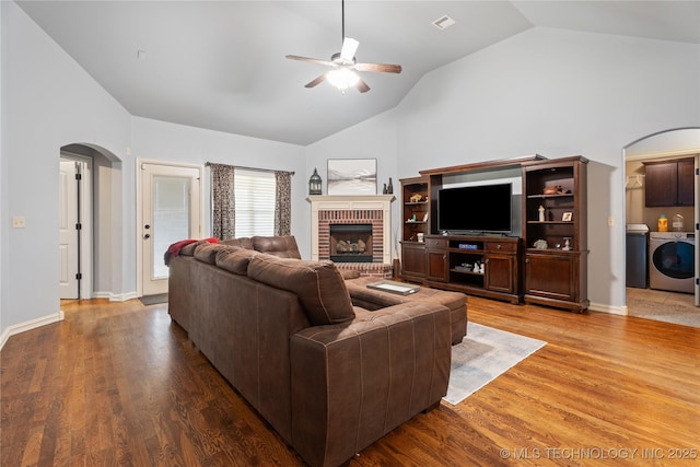3235 Boardwalk Ct, Bartlesville, OK 74006 - living room featuring wood finished floors, arched walkways, washing machine and dryer, a brick fireplace, and ceiling fan